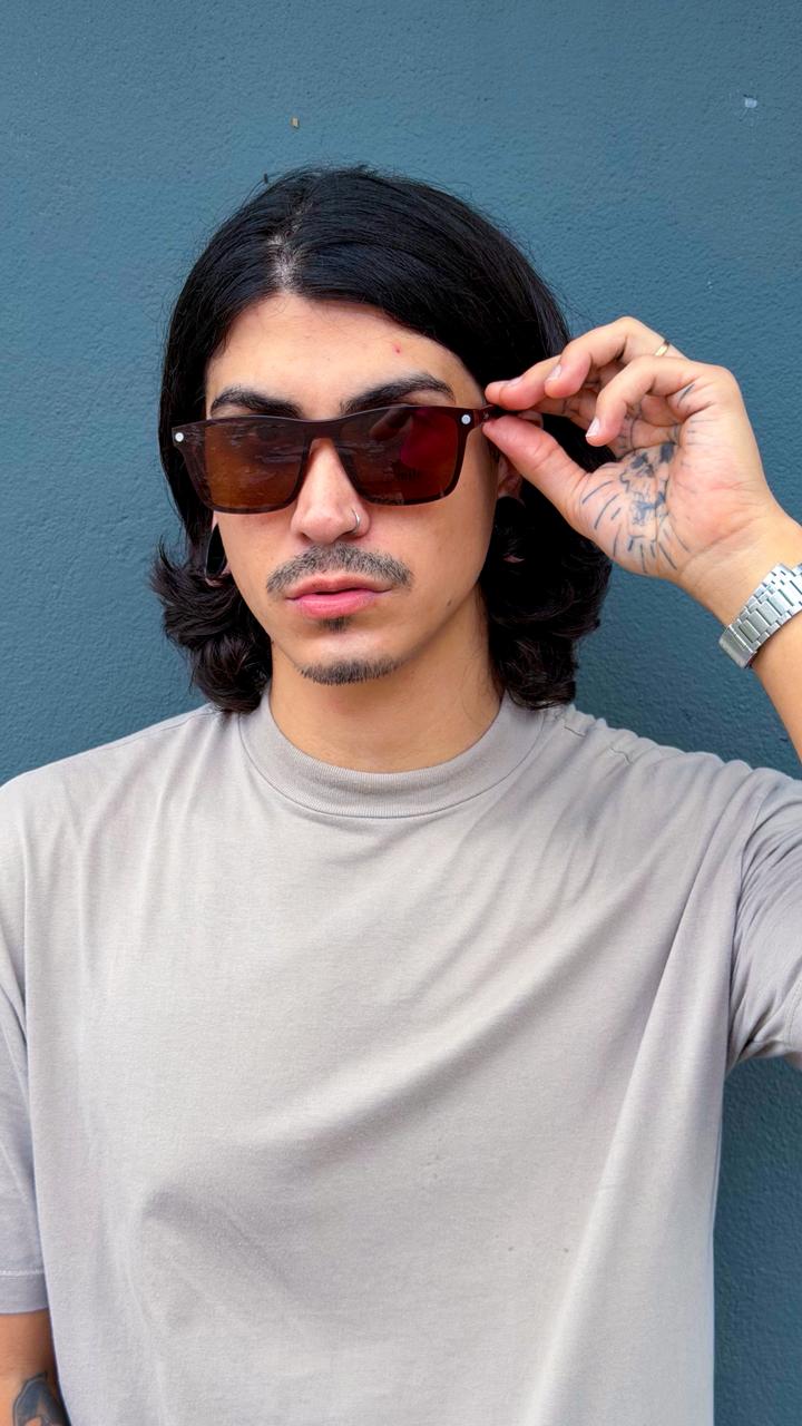 Homem usando óculos de sol com lentes marrons em frente a uma parede azul